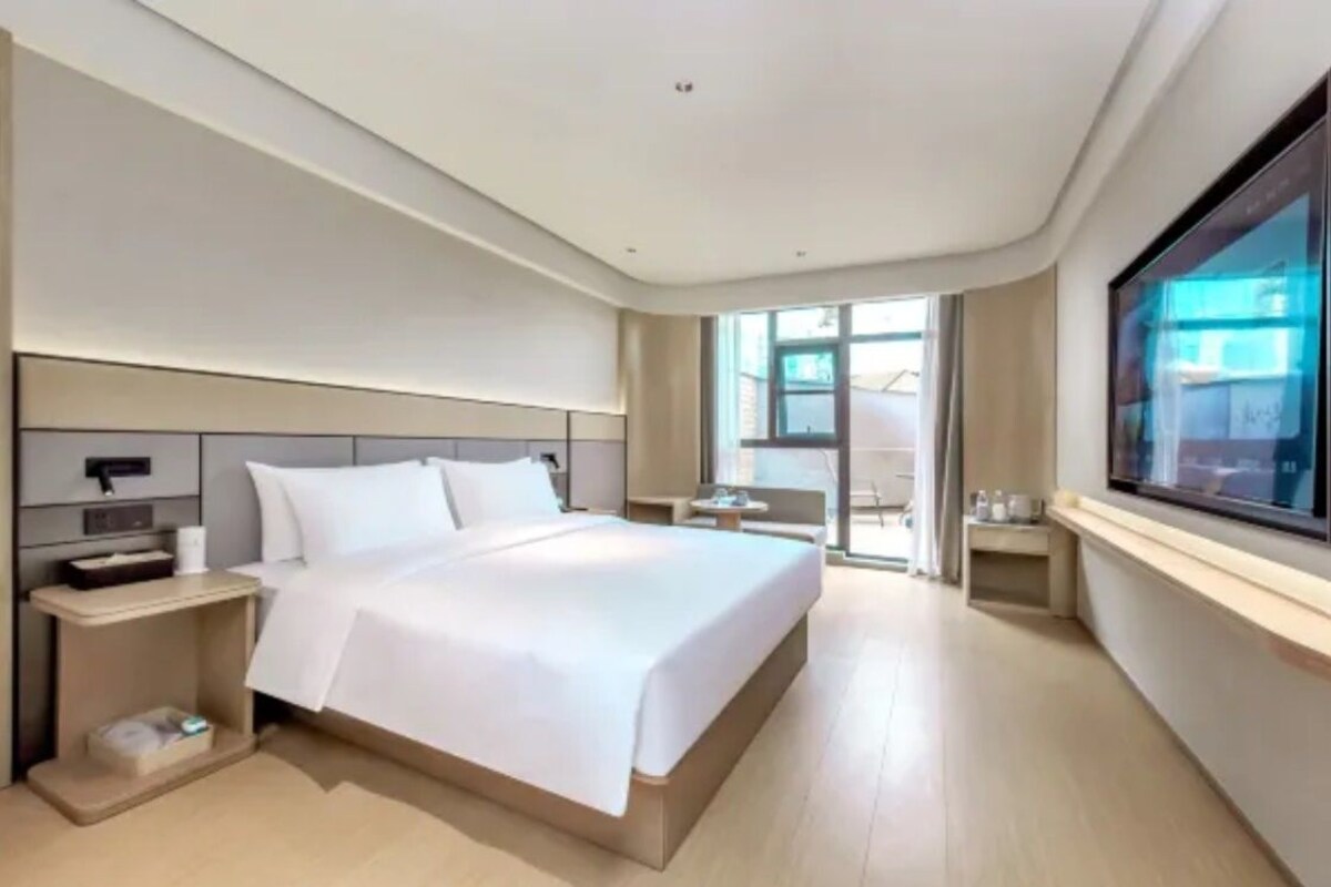 A modern hotel room with a large bed, bedside tables, a desk, and a window with a view.