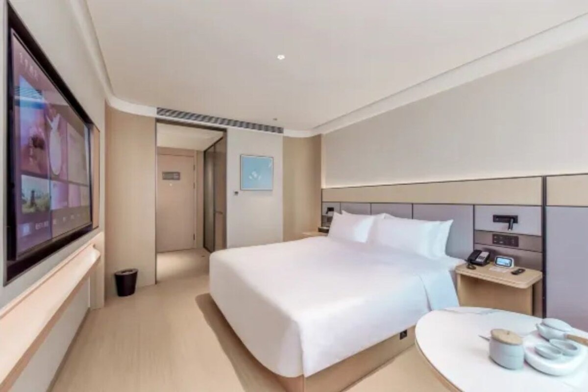Una habitación de hotel moderna con una cama grande, mesitas de noche, un televisor y una pequeña mesa con una taza y un libro.