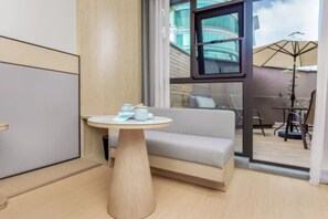 Una habitación de hotel moderna con un sofá, una mesa redonda de madera y vistas al patio exterior.
