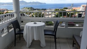 Un balcon avec une table et des chaises, offrant une vue sur le paysage urbain de la côte, avec ses bâtiments et la mer.