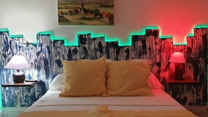 Un lit avec deux oreillers, une table de chevet avec une lampe, et un mur orné d’un tableau et de lumières LED.