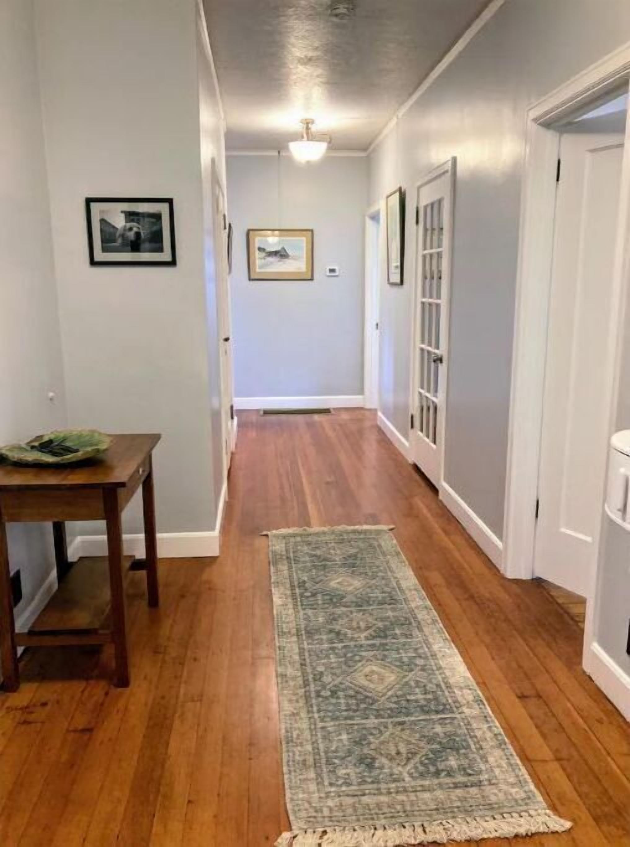 A hallway with wooden flooring, a rug, framed pictures, and a door on the right.