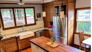 A kitchen with wooden cabinets, a stainless steel refrigerator, a granite countertop, and a window with a view of greenery. - Lida's House, Walk to Everything (Arcata)