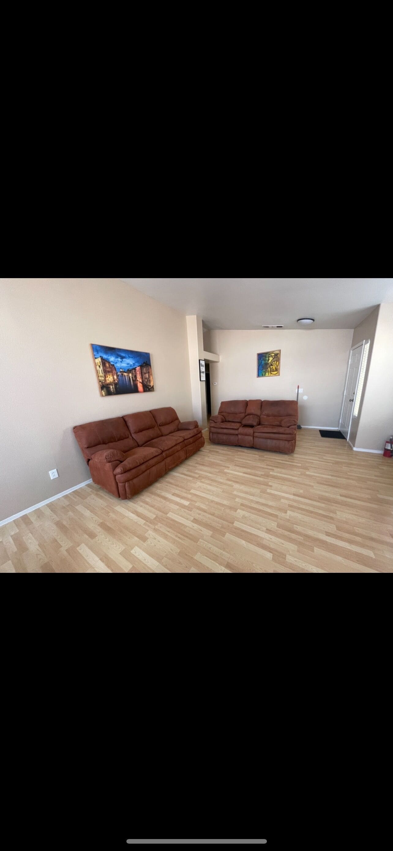 Une pièce avec deux canapés marron, un plancher en bois et deux tableaux accrochés aux murs.