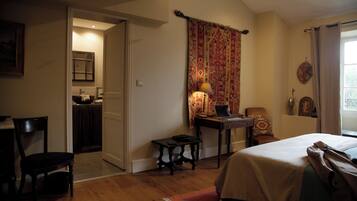 A bedroom with a bed, a desk with a laptop, a chair, a small table, and a window with curtains.