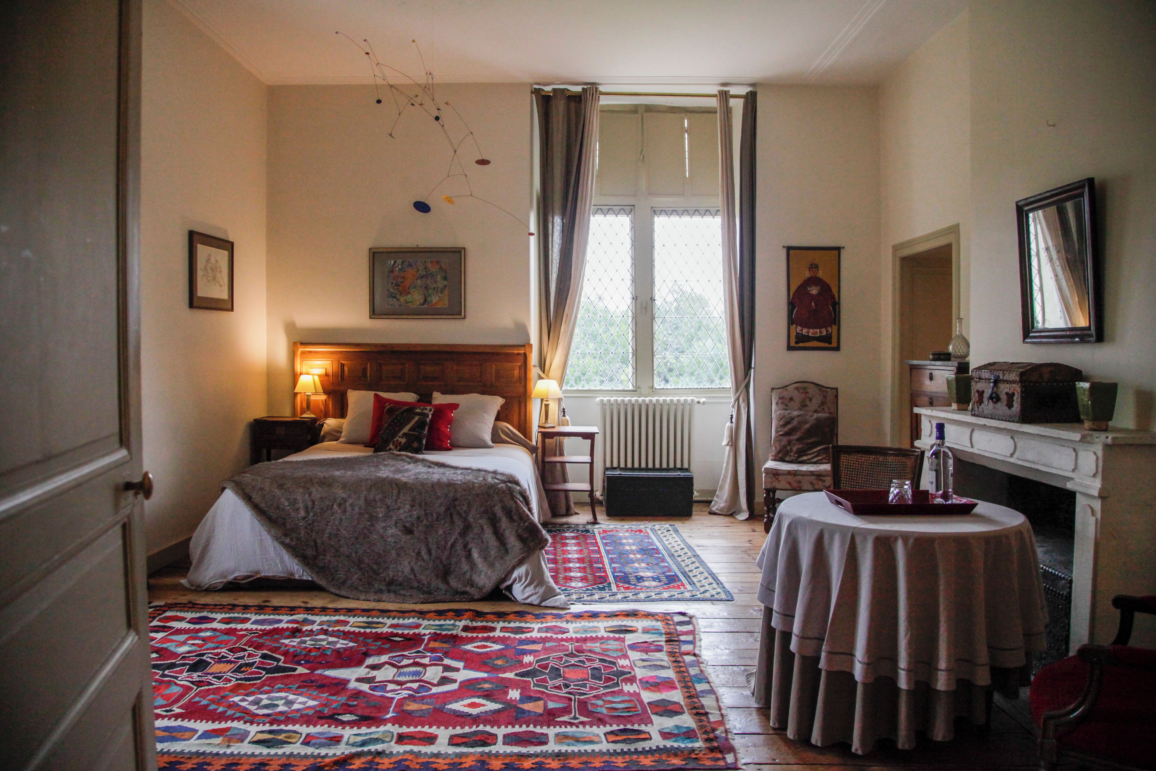 Quarto com cama, mesa de cabeceira, mesa, cadeira, lareira e janela com cortinas.