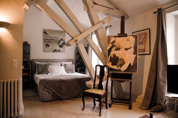Une chambre à coucher avec un lit, une chaise, un tableau accroché au mur et un radiateur.