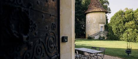 A stone building with a conical roof, a wooden door with intricate metalwork, and a gravel area with a table and chairs.