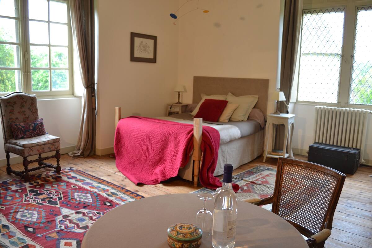 Une chambre à coucher avec un lit, une chaise, une table sur laquelle se trouvent une bouteille et un verre, et une fenêtre avec des rideaux.