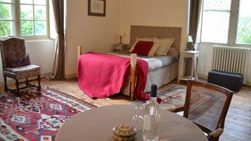 Un dormitorio con cama, una silla, una mesa con una botella y un vaso, y una ventana con cortinas.