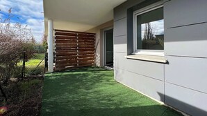 Un bâtiment moderne à l’extérieur gris, avec une clôture en bois et un petit espace verdoyant à l’avant.
