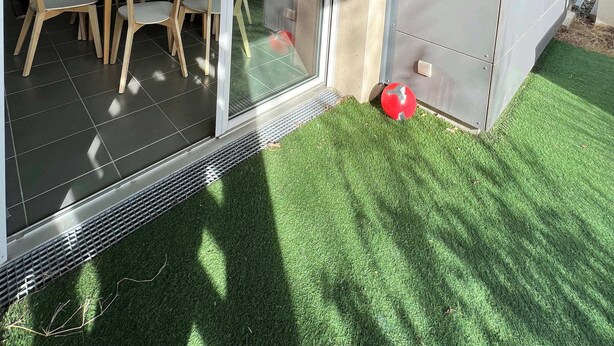 Une cuisine moderne avec un coin repas, une porte-fenêtre coulissante donnant sur un balcon et un petit espace extérieur agrémenté de gazon synthétique.
