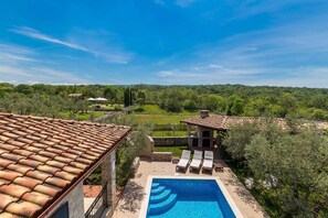 A rooftop pool with a clear view of the surrounding landscape, including a stone building and a grassy area.