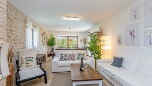 A modern living room with a stone wall, a white sofa, a wooden coffee table, and a dining area with a view of greenery.