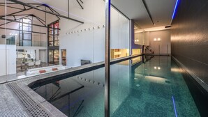 En indendørs swimmingpool med glasvæg, en moderne trappe og et loungeområde med siddepladser.
