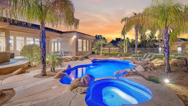 A swimming pool with a stone deck, surrounded by palm trees and a house with large windows. - Desert Oasis ★Pool-Spa-Disc Golf-Ping Pong-Poker Table-Pool Table★ (Scottsdale)