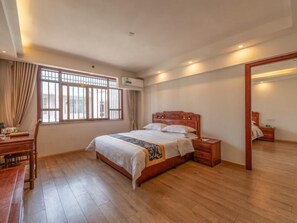 A bedroom with a wooden bed, a desk, a chair, and a large window with curtains.