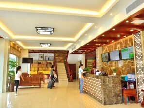 A hotel lobby with a reception desk, a staircase, and a seating area.