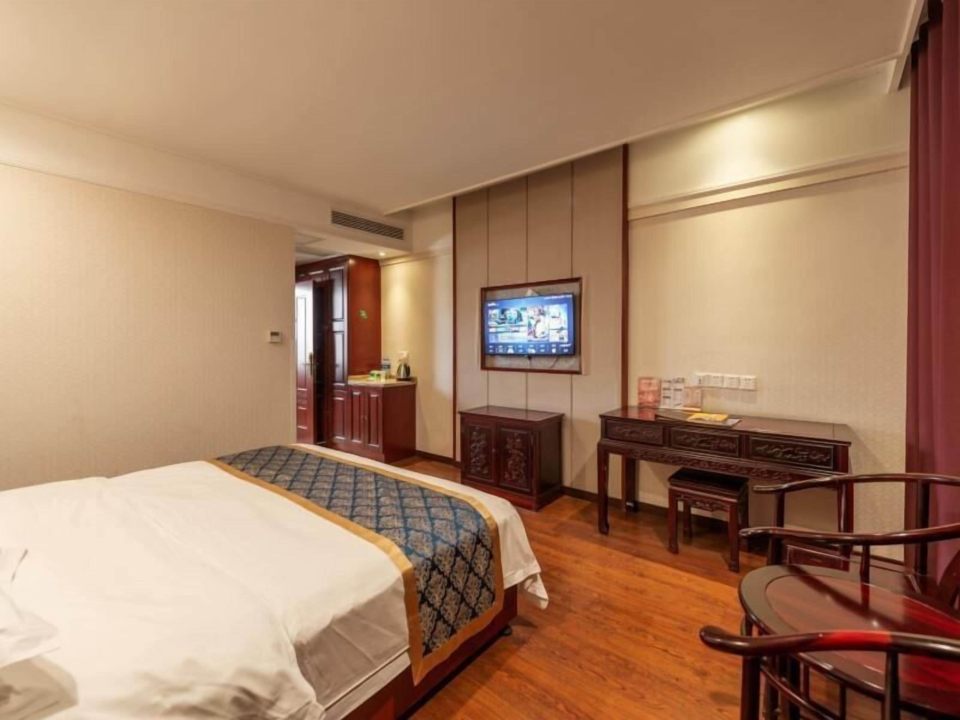 Una habitación de hotel con cama, escritorio, silla, televisor y armario.