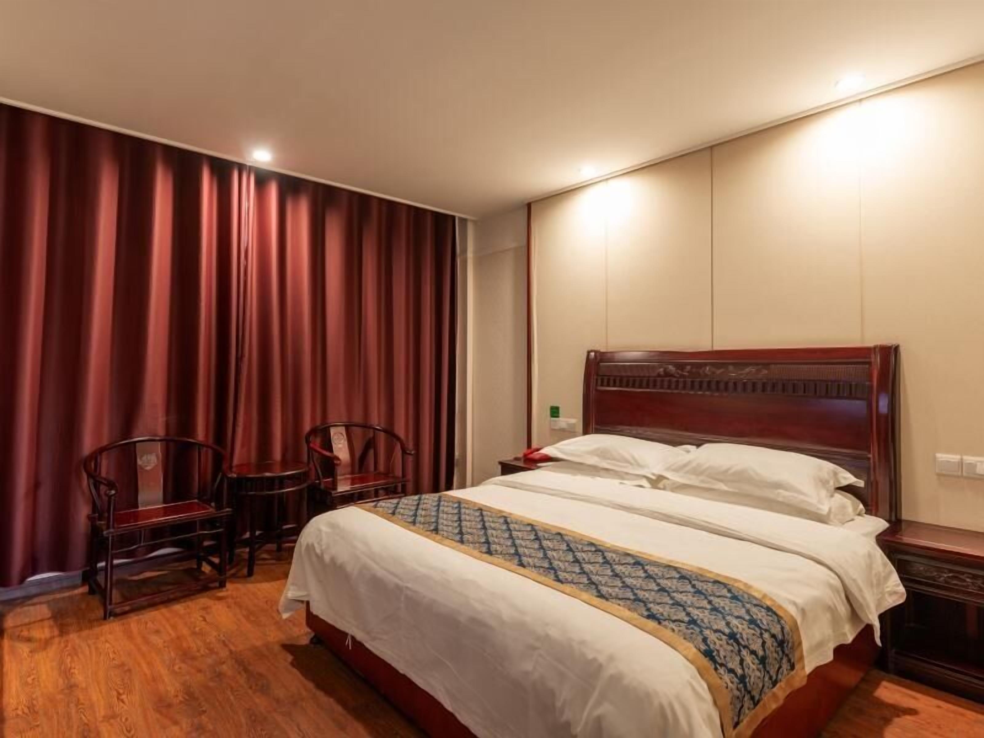 A hotel room with a large bed, two wooden chairs, a red curtain, and a wooden headboard.