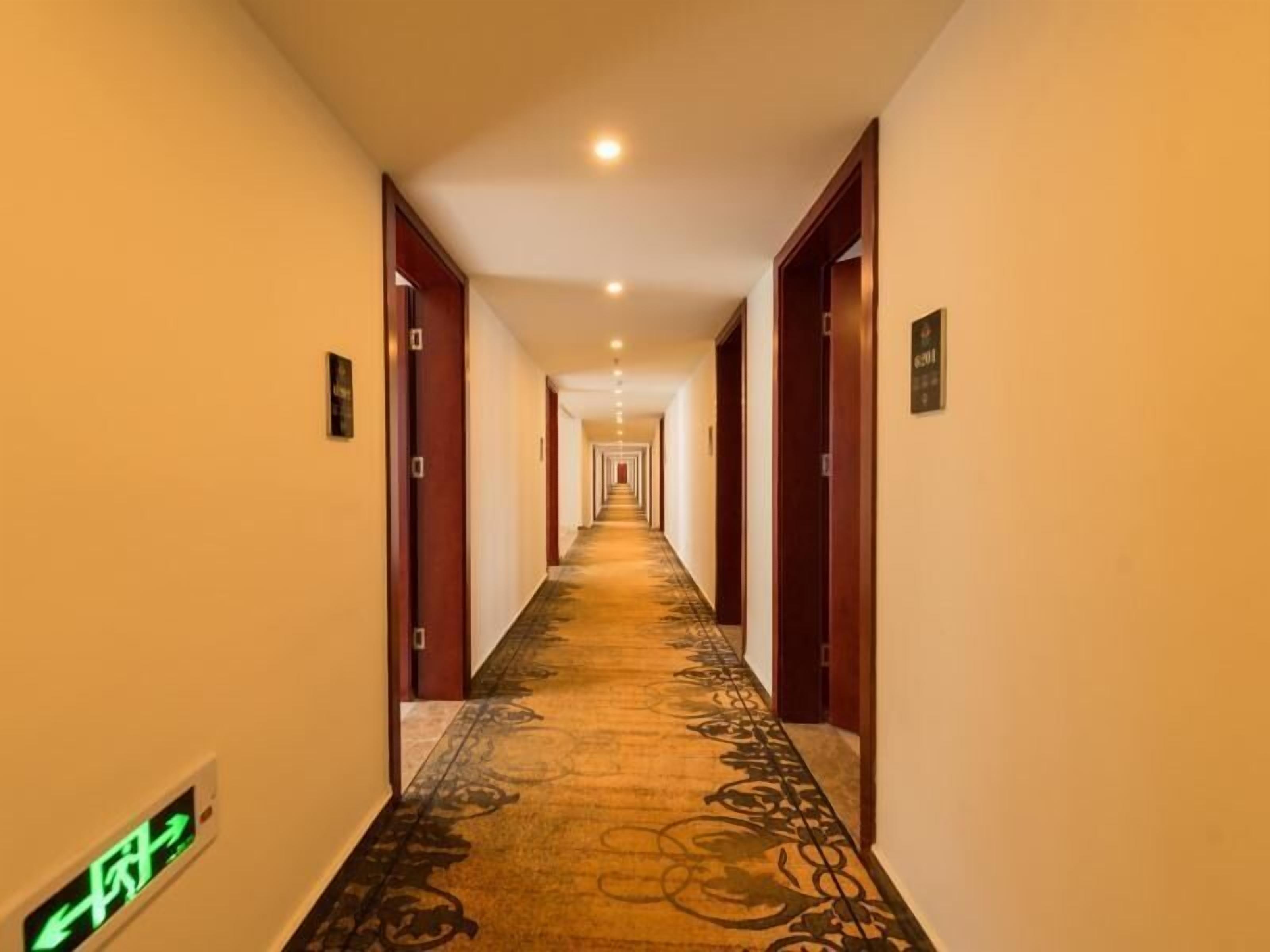 A hotel hallway with a carpeted floor, wooden doors, and a sign indicating the direction to the exit.