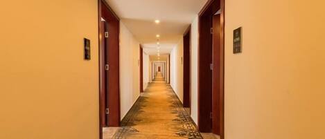 A hotel hallway with a carpeted floor, wooden doors, and a sign indicating the direction to the exit.