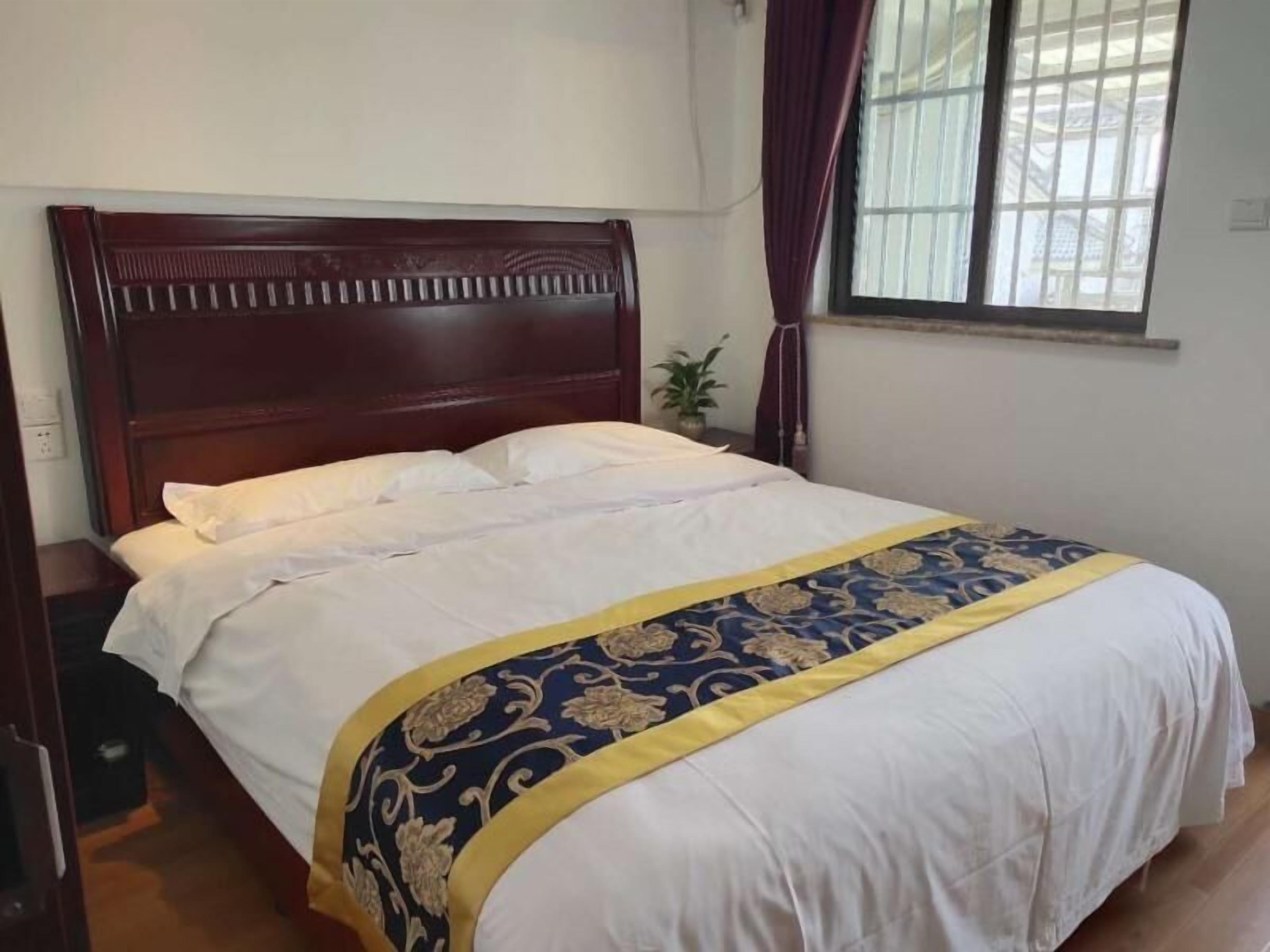 A neatly made bed with a white and blue patterned bedspread, a wooden headboard, and a window with curtains.