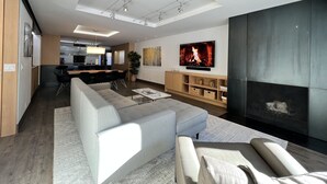 A modern living room with a large TV, a fireplace, and a dining area with a kitchen in the background. - monarch chalet aspen condo (Aspen)