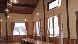 Un interior de madera con una larga mesa, bancos, ventanas amplias y lámparas colgantes.