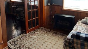 A rustic room with a wooden ceiling, a large window, a bed, a television, and a clock on the wall. - Tiny Cabin in Huron National Forest! (Luzerne)