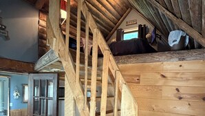 A wooden staircase leading to a loft bedroom with a bed and a small table. - Tiny Cabin in Huron National Forest! (Luzerne)