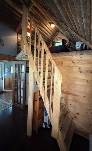 Eine Holztreppe führt zu einem Schlafzimmer auf einer Empore, mit einem Bett und einem kleinen Tisch.