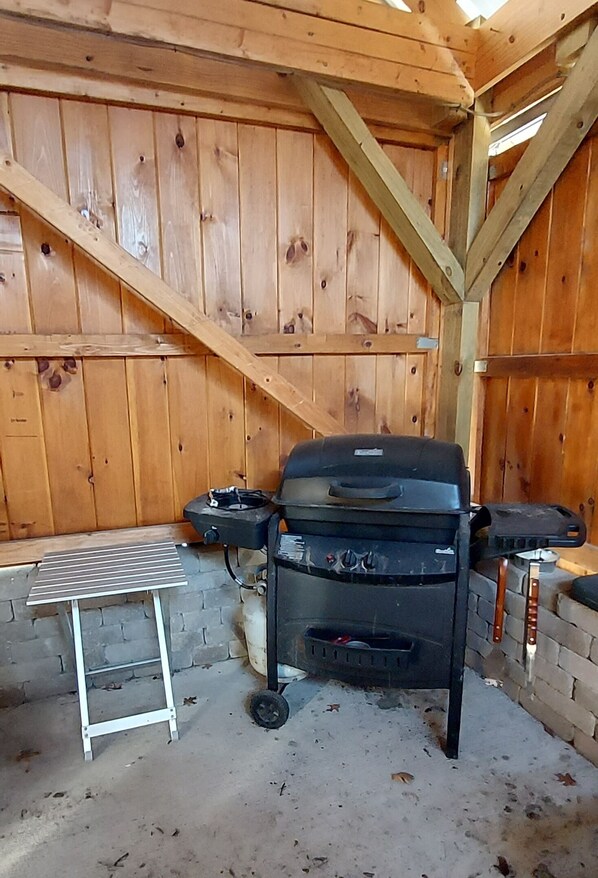 A wooden interior with a barbecue grill, a small metal table, and a brick wall. - Tiny Cabin in Huron National Forest! (Luzerne)