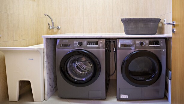 A compact laundry area with two front-loading washing machines, a small white basin, and a basket on top.