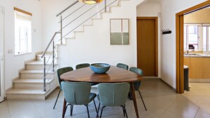 A dining area with a round wooden table, six chairs, a bowl, a staircase, and a kitchen visible through an open door.