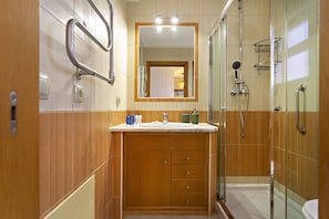 Une salle de bain avec des lambris en bois, un lavabo avec des articles de toilette, un miroir et une douche séparée par une paroi en verre.