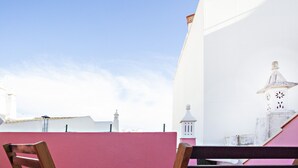 A view of a building with a pink wall and a white facade, featuring a tower with a pointed roof and a clock.