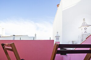 Vista de un edificio con pared rosa y fachada blanca, que presenta una torre con techo puntiagudo y un reloj.