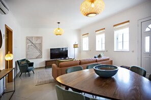 Una sala de estar moderna con una mesa de comedor de madera, sillas verdes, un sofá y un televisor.