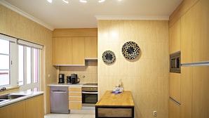 A compact kitchen with wooden cabinets, a dishwasher, an oven, and a microwave. There is a window with blinds, a wooden table, and two decorative plates on the wall.
