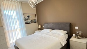 Een slaapkamer met een groot bed, een nachtkastje met een lamp, een bijzettafeltje met een vaas en een schilderij aan de muur.