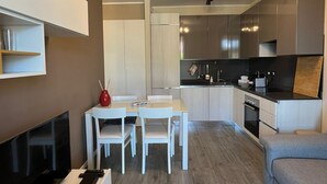 Een moderne keuken met witte kastjes, een eettafel met stoelen en een televisie links.