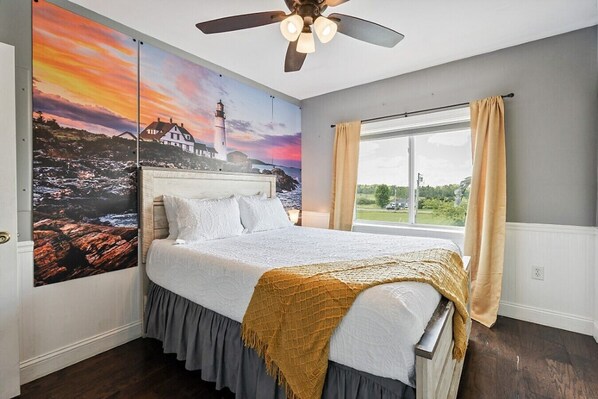 A bedroom with a large bed, a ceiling fan, a window with curtains, and a wall mural.