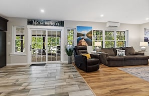A living room with a fireplace, a sofa, a recliner, and a large window with a view of trees.