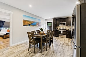 A modern kitchen with dark cabinets, stainless steel appliances, and a dining area with a wooden table and chairs. - Riverside Getaway w/HotTub | 3 (Brewer)