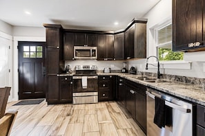 A modern kitchen with dark cabinetry, stainless steel appliances, and a marble countertop.