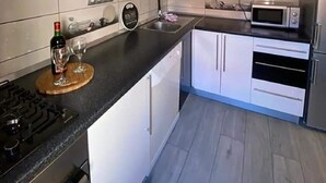 A modern kitchen with white cabinets, a black countertop, a microwave, and a wine bottle. - Lavanda Penthouse - Three Bedroom Apartment (Kastel Luksic)
