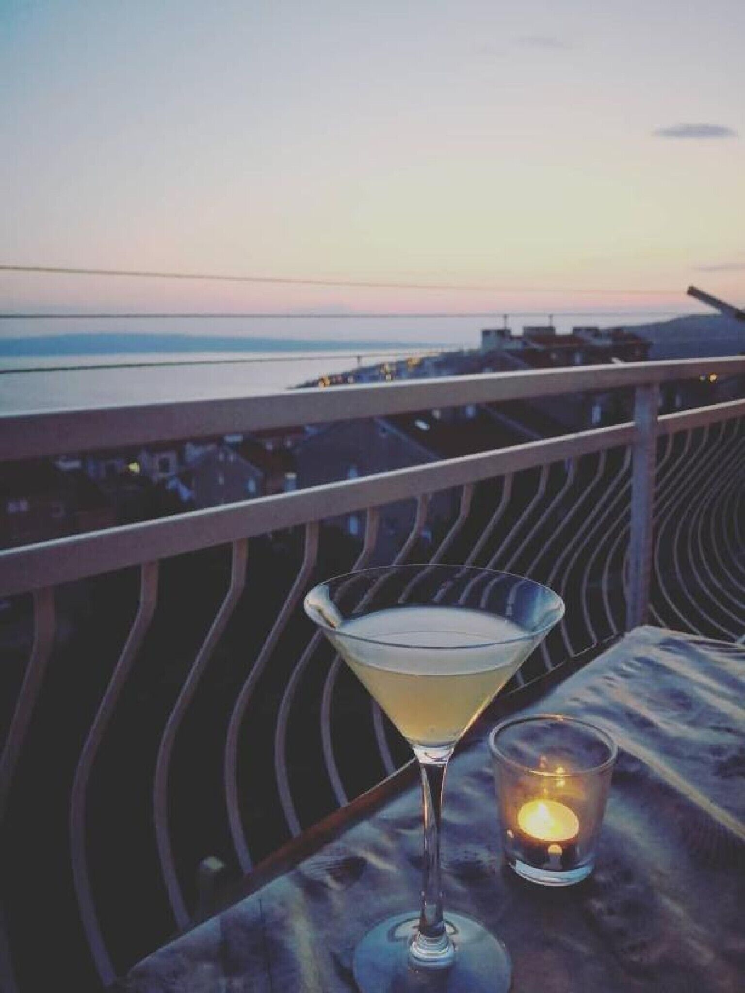 Ein Balkon mit Blick auf das Meer bei Sonnenuntergang, ein Martini-Glas und eine Kerze.