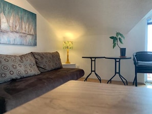 Una habitación acogedora con un sofá marrón, una mesita redonda pequeña, una lámpara y una planta en maceta.