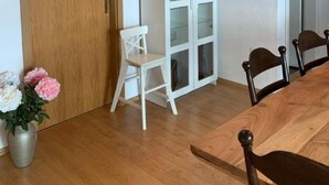 A room with a wooden door, a white cabinet with glass doors, a dining table with chairs, and a potted plant.